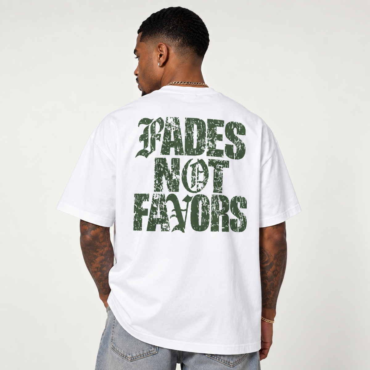 Model seen from behind wearing theCut Fades Not Favours tee in white, showing the large green distressed FADES NOT FAVORS block lettering across the back.