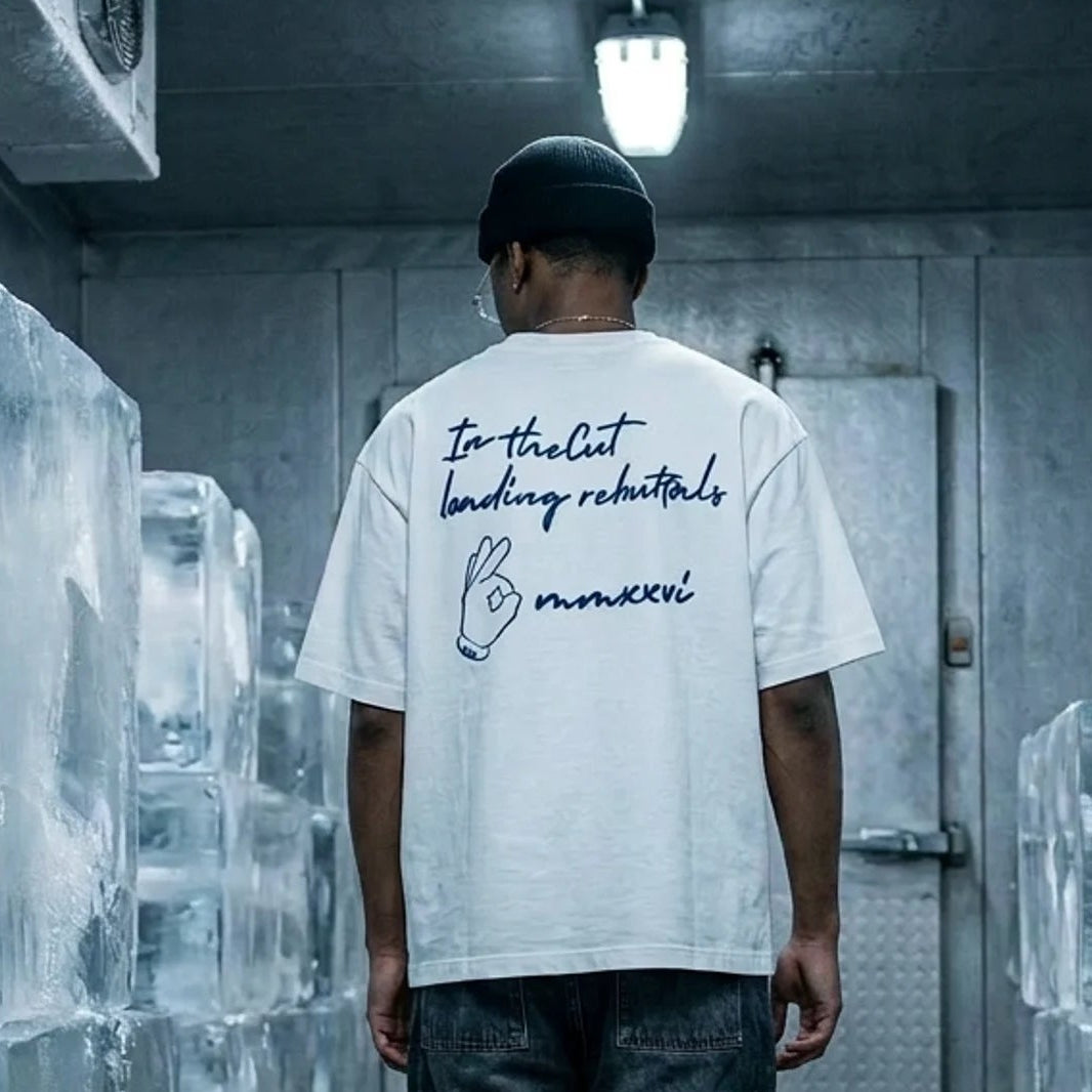 Model wearing theCut Loading Rebuttals oversized tee in white in a graffitied alleyway.