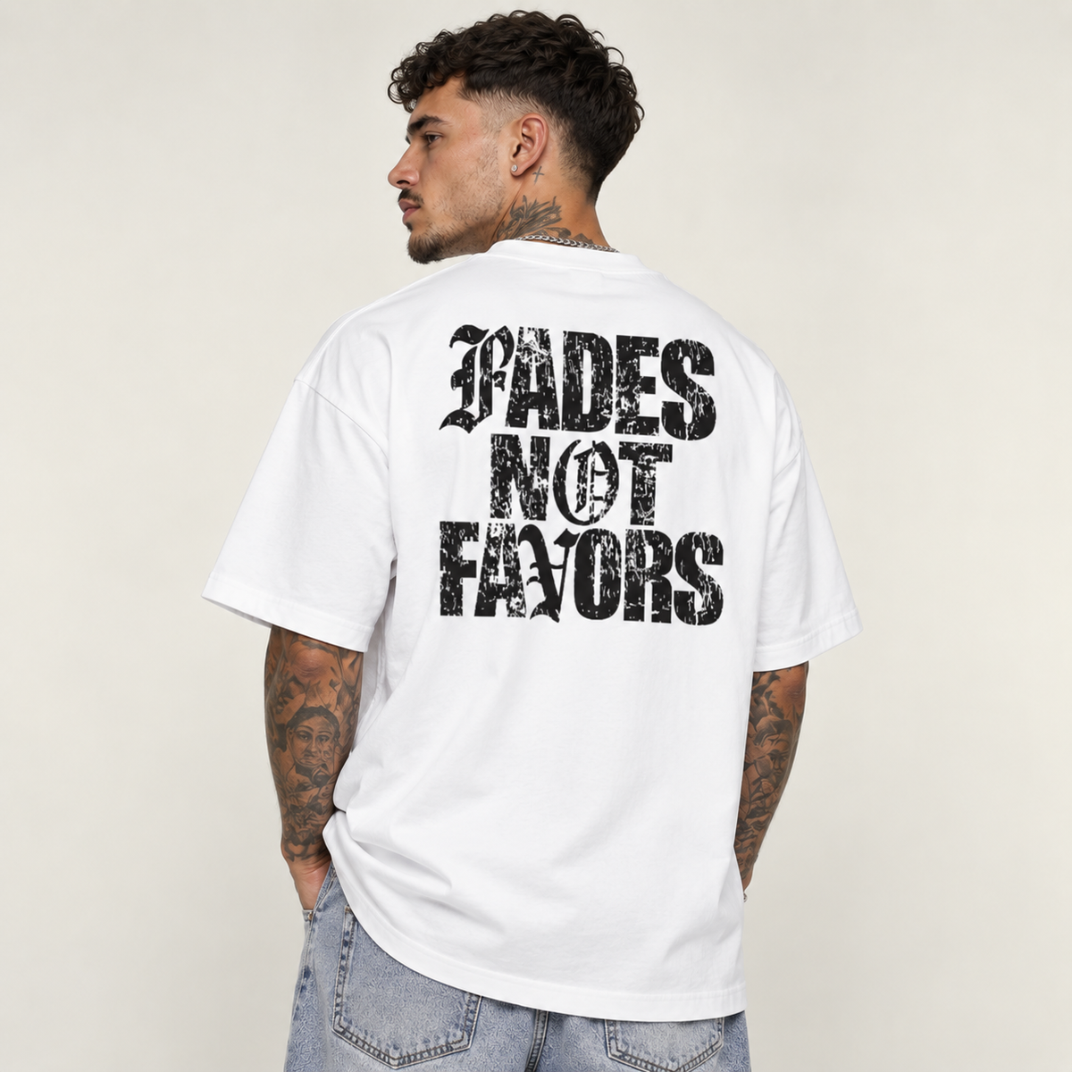 Model seen from behind wearing theCut Fades Not Favours tee in white, showing the large black distressed FADES NOT FAVORS block lettering across the back.