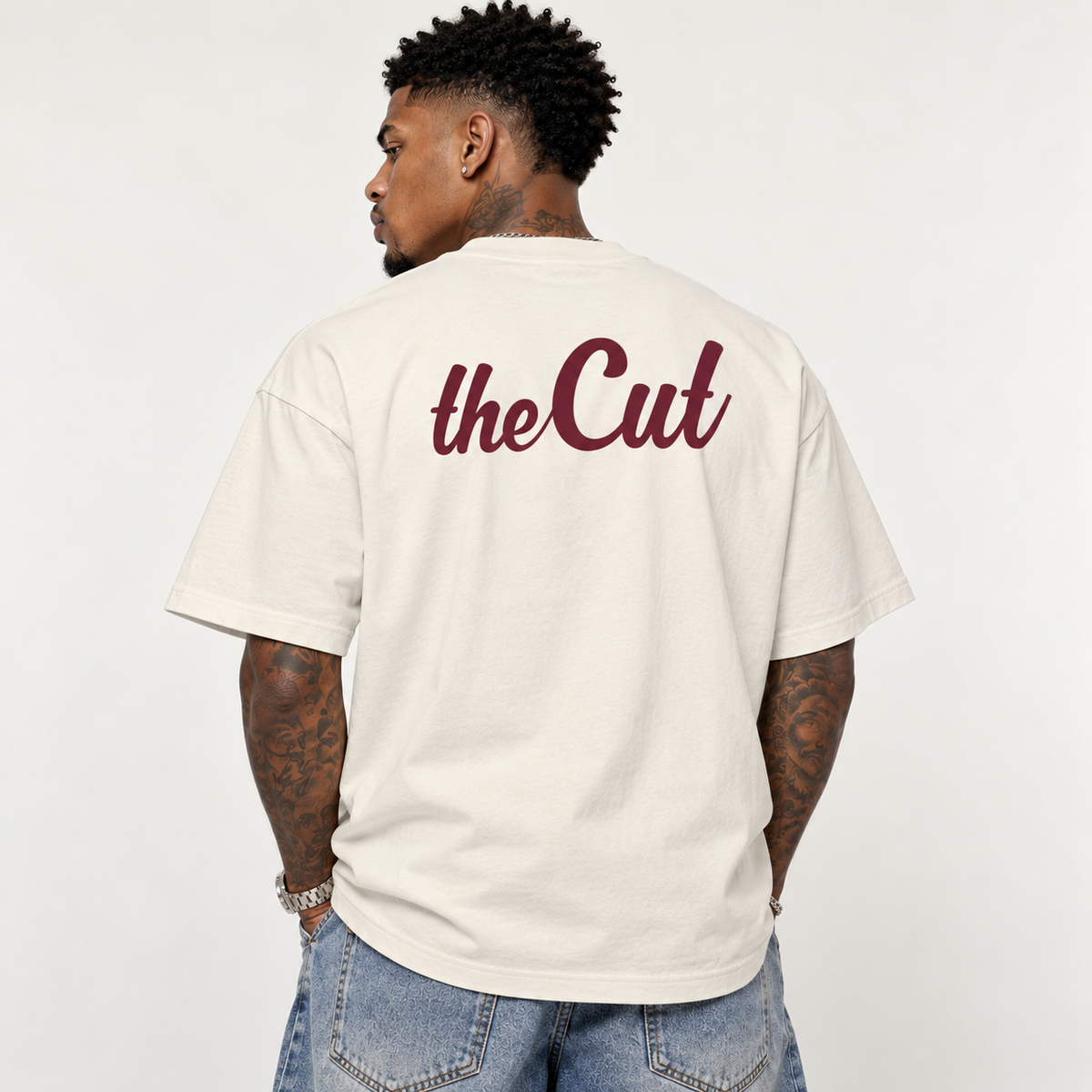 Model seen from behind wearing theCut TC tee in beige, showing the large burgundy theCut script across the back.