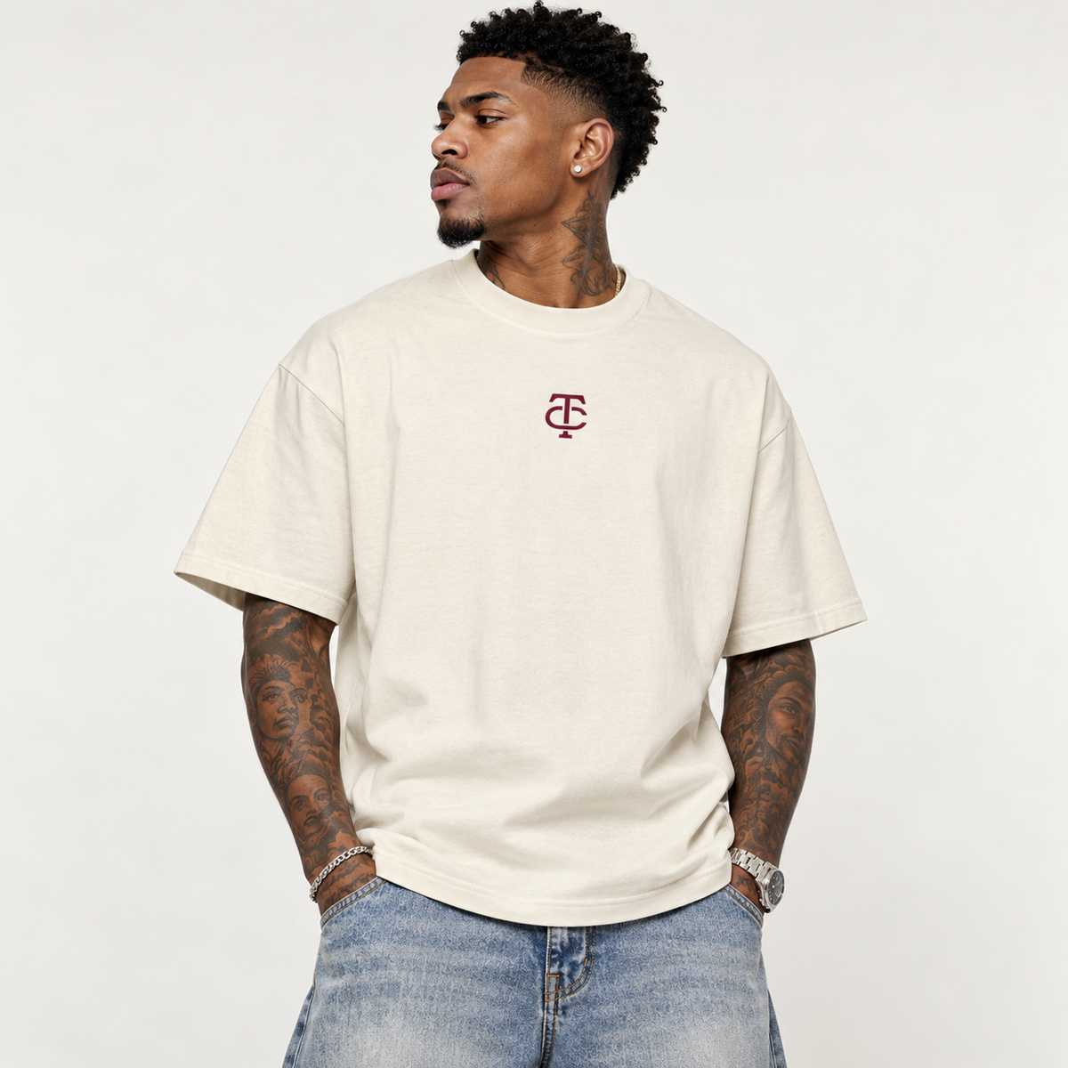 Model wearing theCut TC tee in beige, front view, with a small burgundy TC monogram embroidered at the left chest.