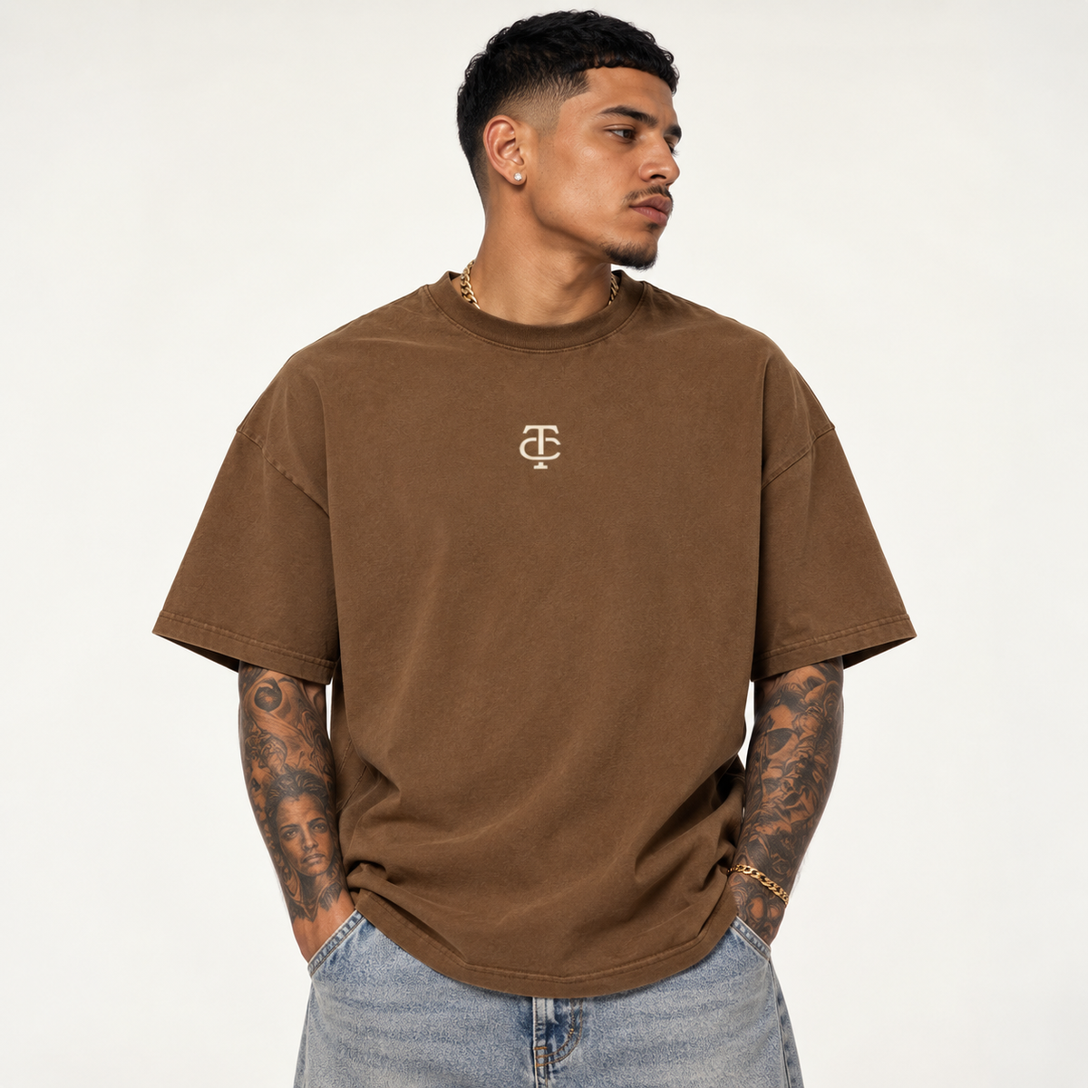 Model wearing theCut TC tee in washed brown, front view, with a small cream TC monogram at the left chest.