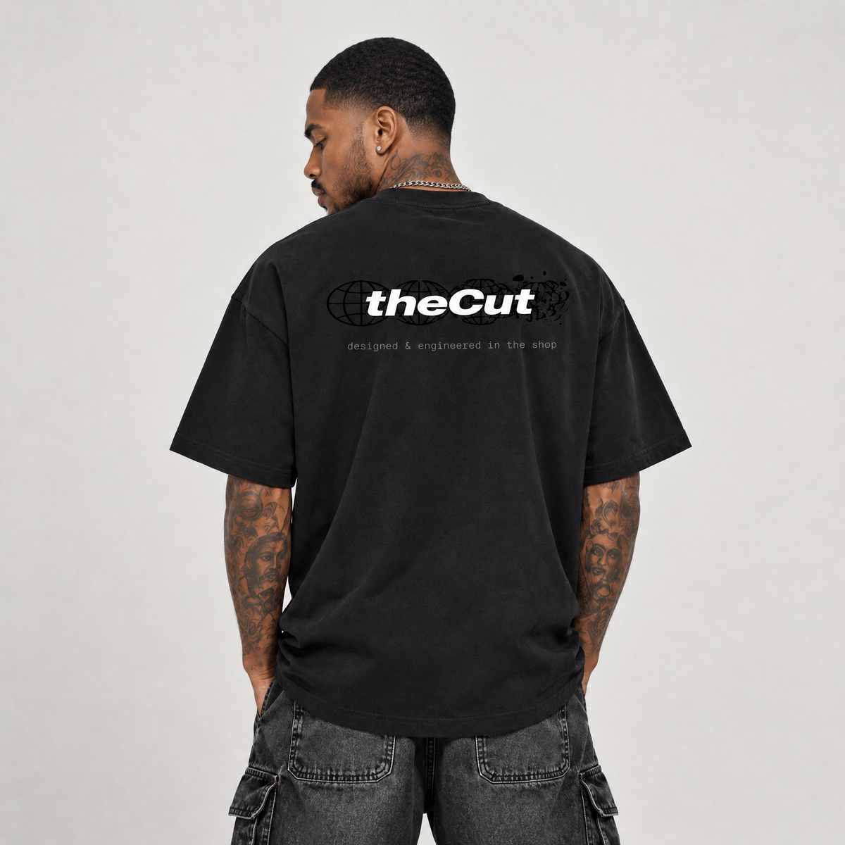 Model seen from behind wearing theCut Globe tee in black, showing the large white theCut wordmark and small caption printed across the back.