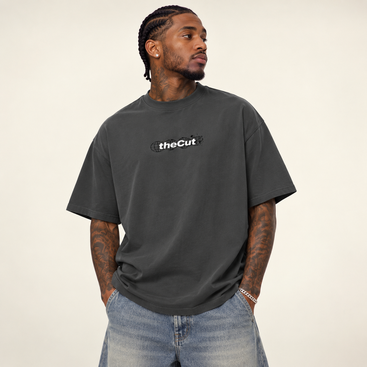 Model wearing theCut Globe tee in charcoal grey, front view, with a small white theCut wordmark at the left chest.