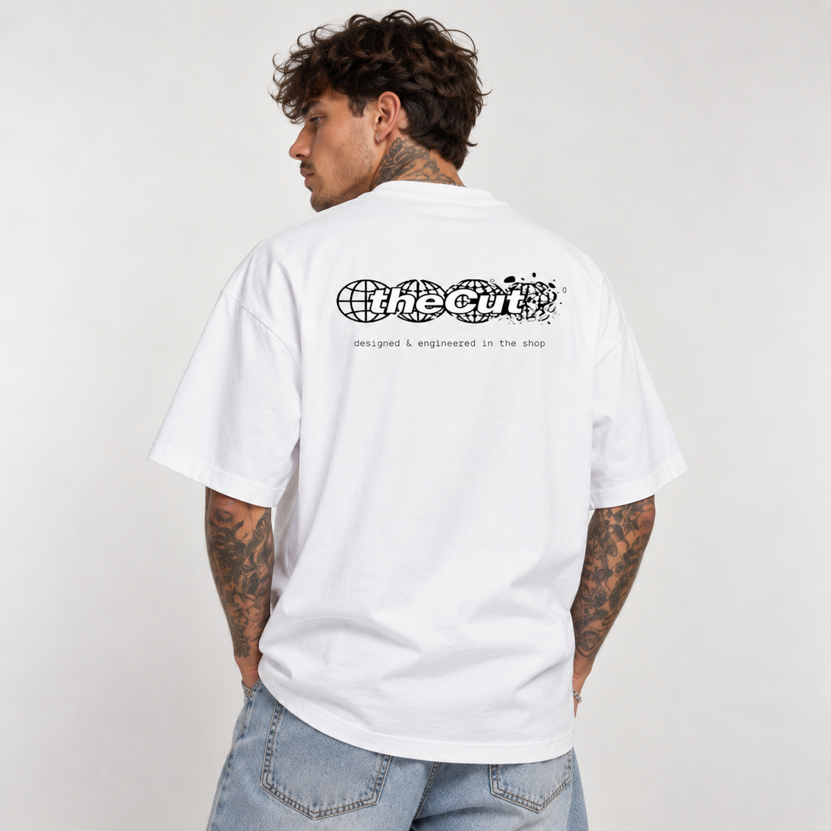 Model seen from behind wearing theCut Globe tee in white, showing the large black theCut wordmark and small caption printed across the back.