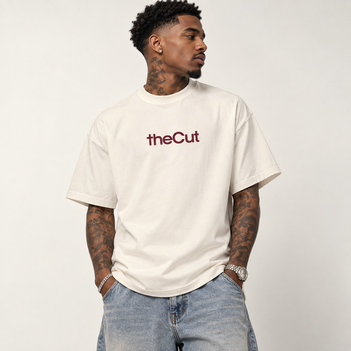 Model wearing theCut tee in beige, front view, with a small burgundy theCut wordmark at the left chest.