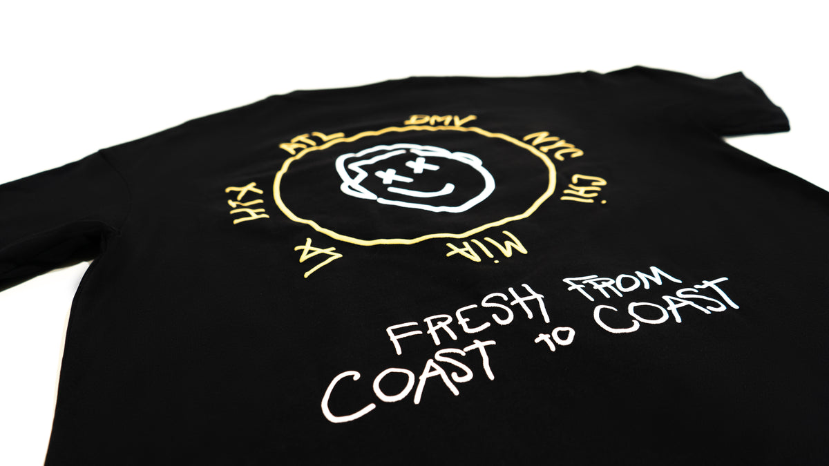Close detail of theCut Anywhere tee in black, showing the yellow Fresh From Coast To Coast circular print.
