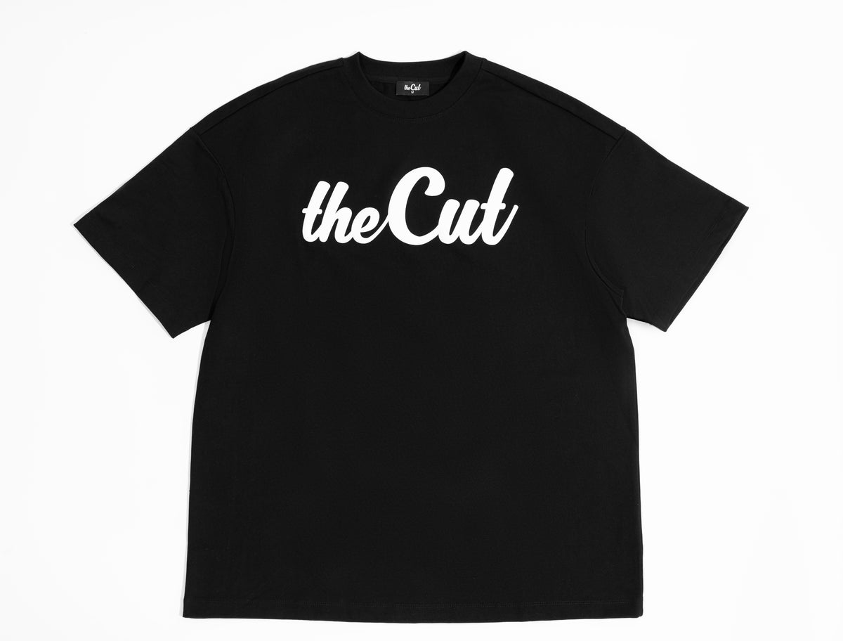 theCut Puffed Logo tee in black shown flat from the front, with the raised white theCut script logo.